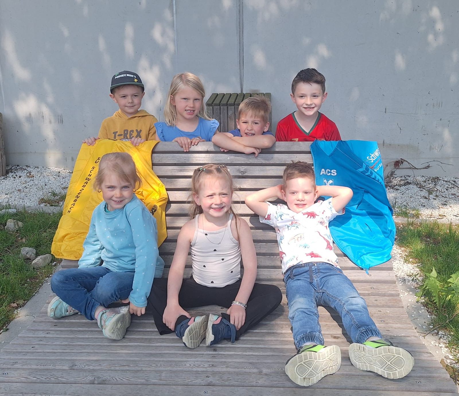 Kinder des absolvierten Kinderschwimmkurses sind auf einer Bank abgebildet.