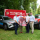 Zwei Autos mit 4 Personen im Vordergrund die ein Plakat über Wladbrandgefahr halten