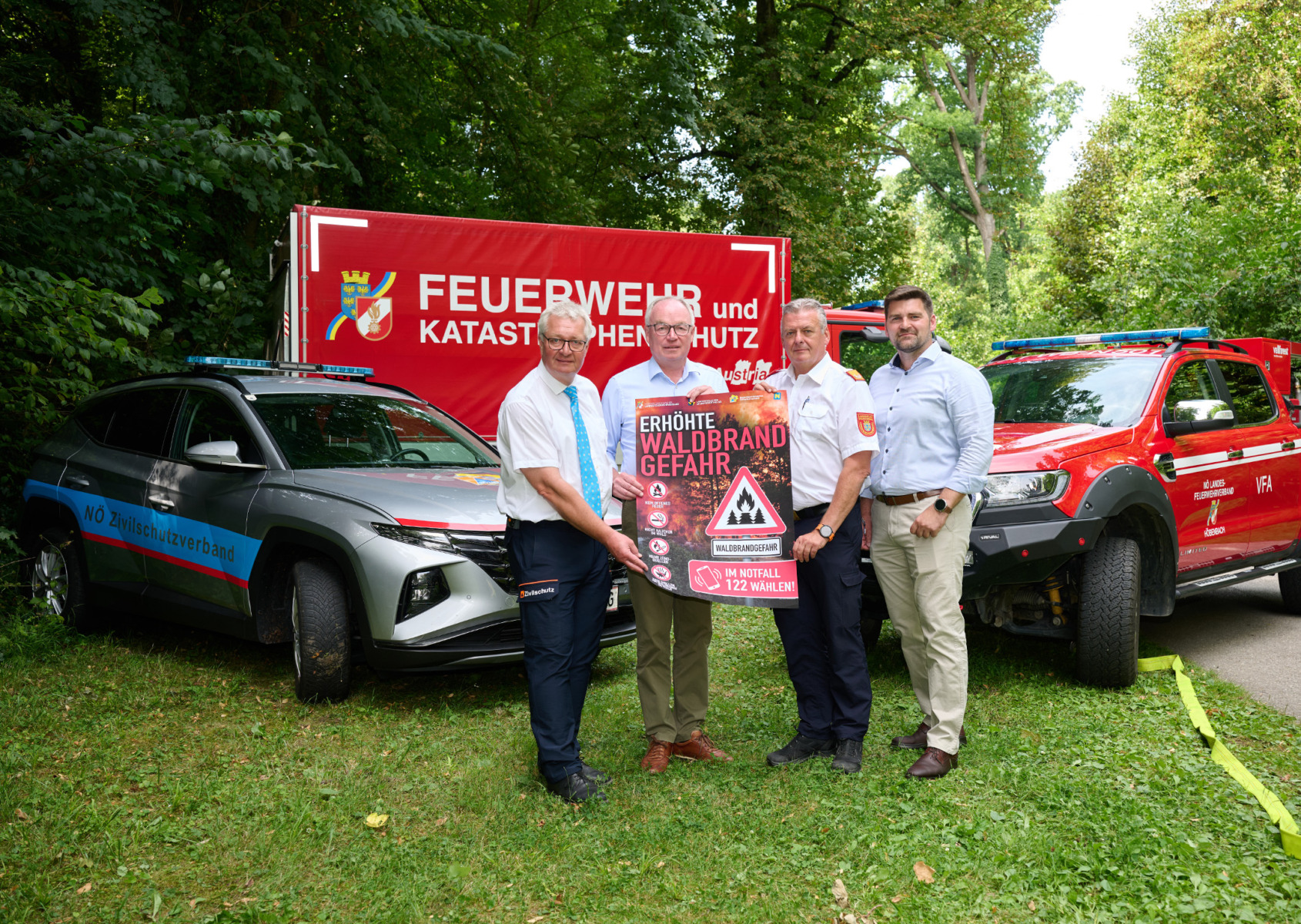 Zwei Autos mit 4 Personen im Vordergrund die ein Plakat über Wladbrandgefahr halten